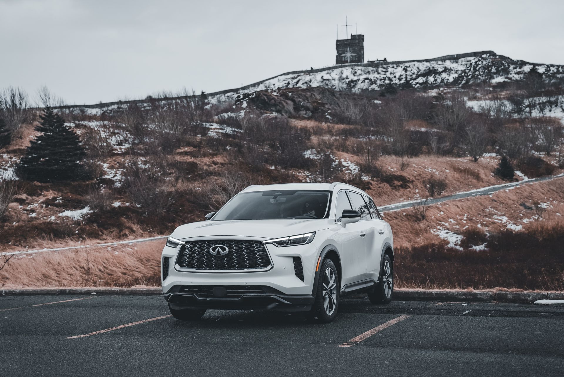 White SUV parked on a road with snow-covered hills in the background during winter conditions